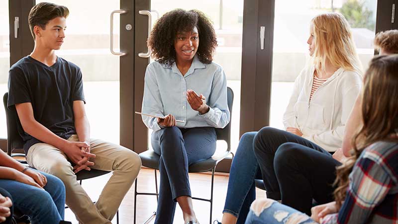 Female tutor leading discussion group amongst high school pupils